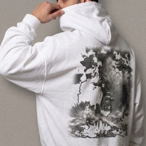A man wearing the relaxed-fit hoodie in white, seen from behind, showing the ABYSS design printed across the back: a tall-masted ship heeled over against rising swell and closing storm, in monochrome greys.